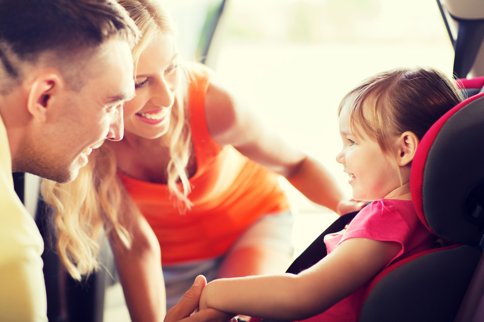 family, transport, safety, road trip and people concept - happy parents talking to little girl in baby car seat