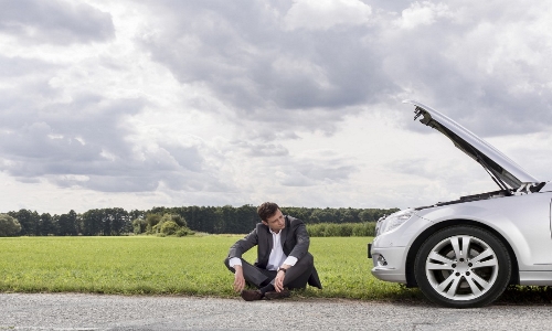 A man sitting on the ground next to his broken down car