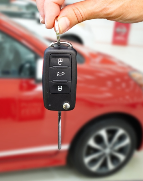 Hand giving car keys in front of red car